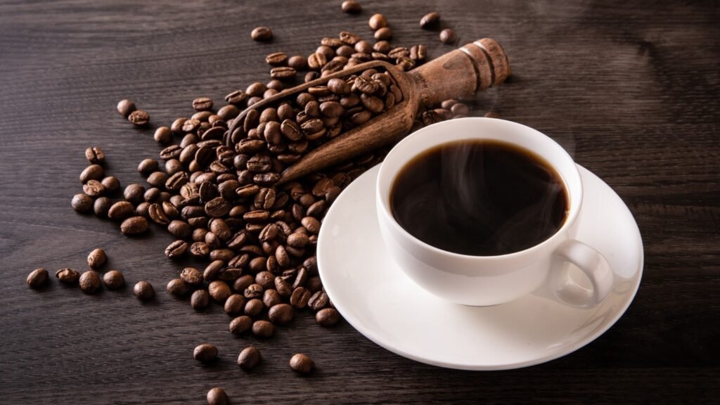 A cup of black coffee with some coffee beans placed on a wooden table